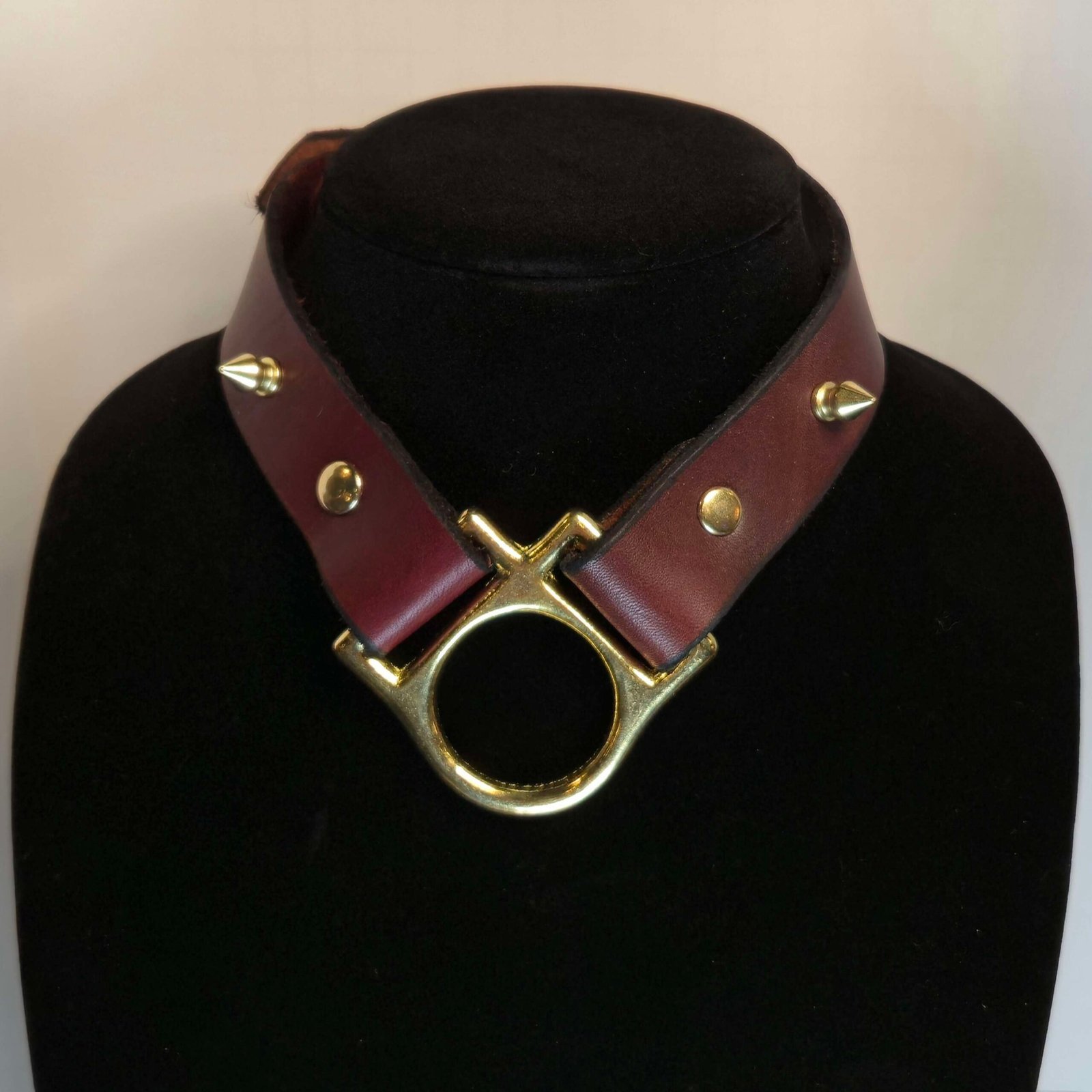 Handcrafted leather collar with gold-tone hardware, featuring spikes and a central O-ring, displayed on a black mannequin.