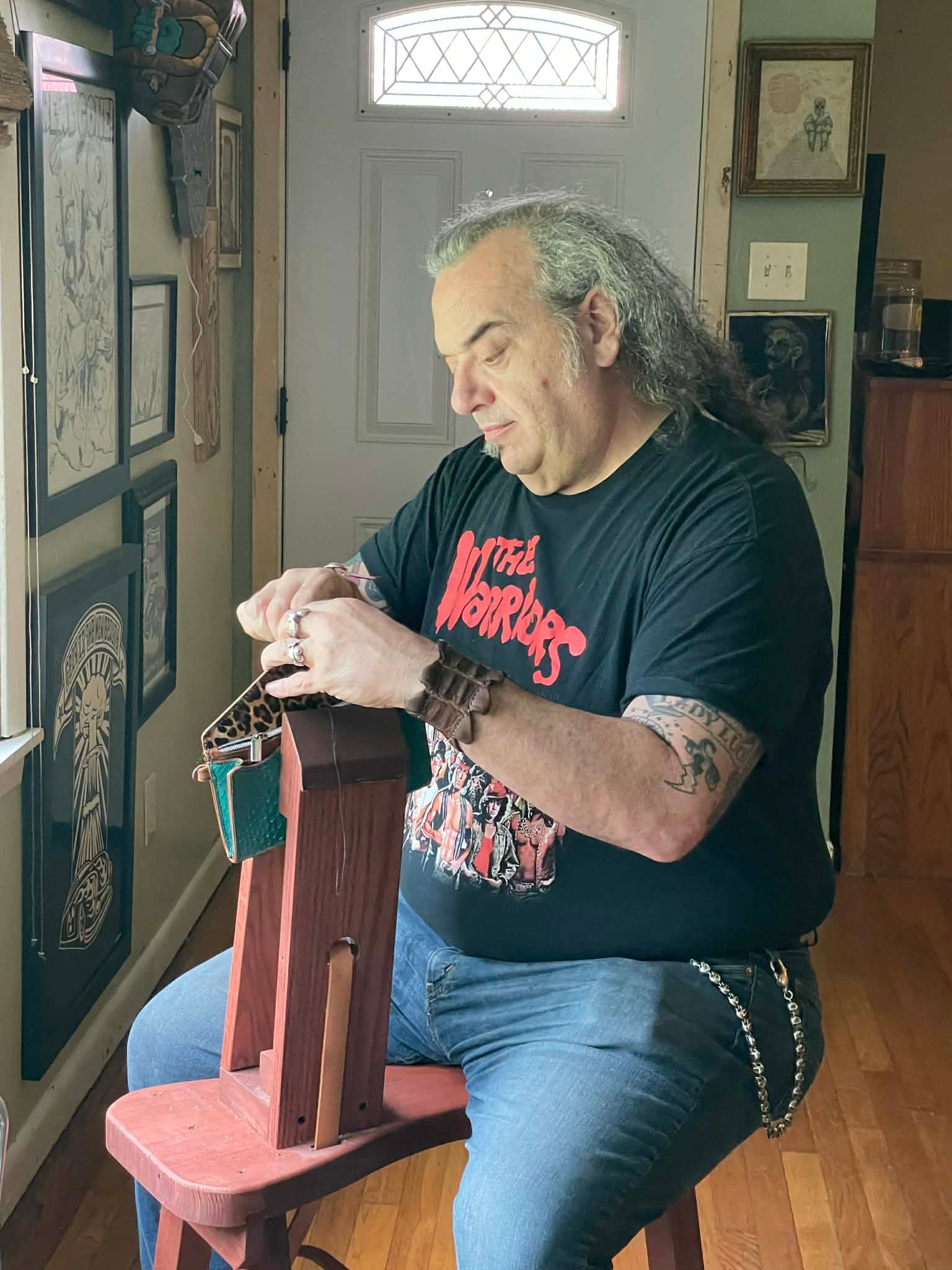 Mike Menard, lead artisan at W.E.L.P., crafting unique leather goods on a wooden stool, surrounded by artwork and natural light, showcasing his artisan craftsmanship.