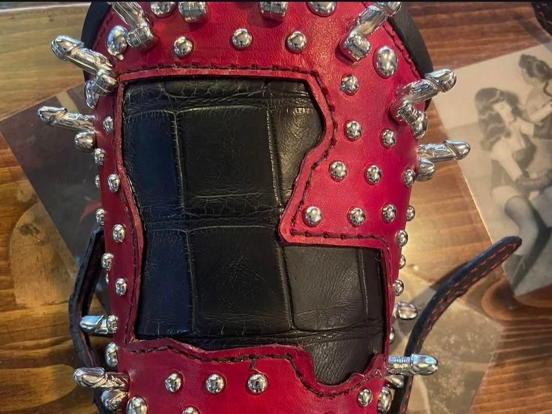 Handcrafted leather paddle with red and black sections, adorned with silver studs and spikes, showcasing W.E.L.P.'s artisan craftsmanship in unique BDSM gear.