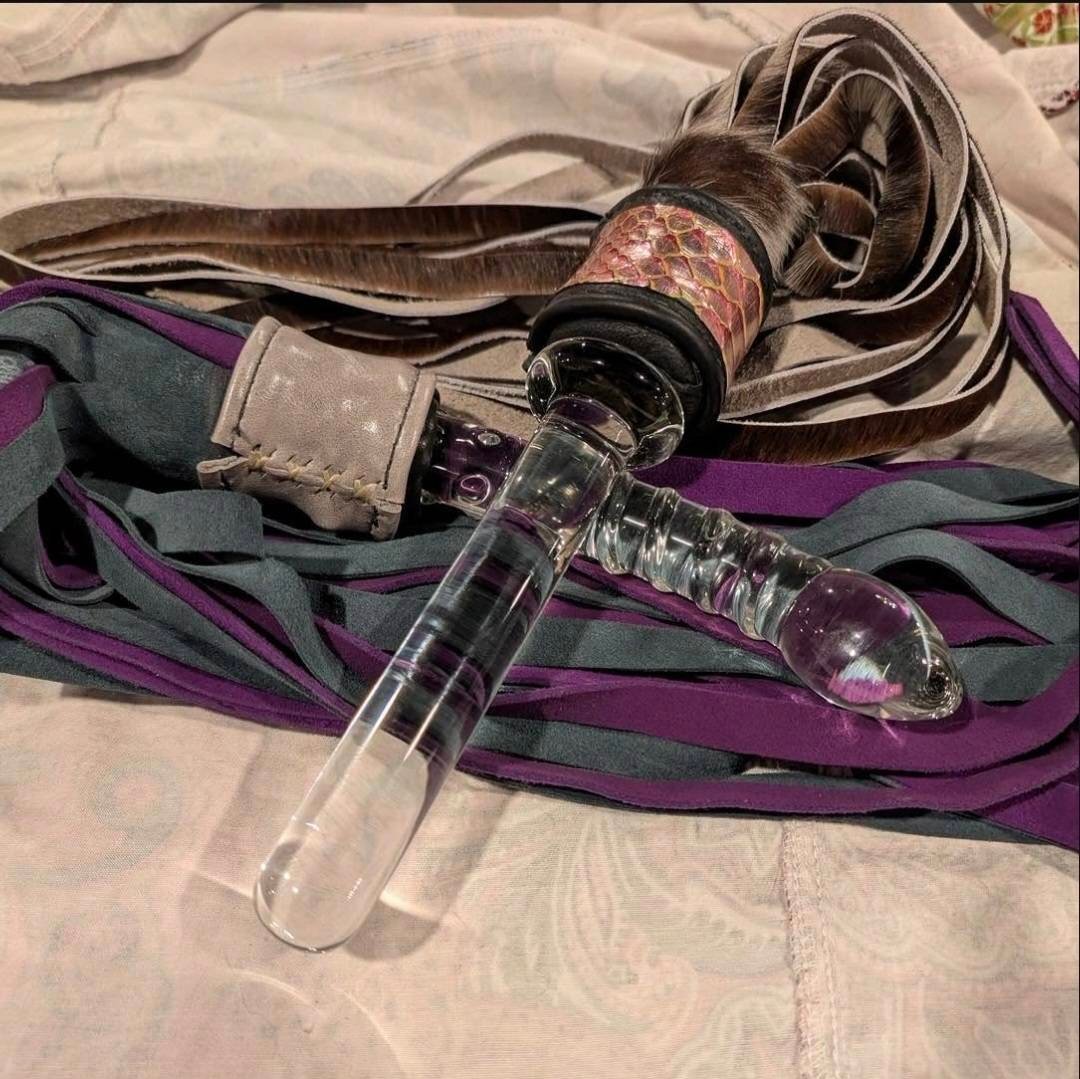 Handcrafted impact toys including a custom flogger with premium leather tails and a glass wand, showcasing artisan craftsmanship by W.E.L.P.