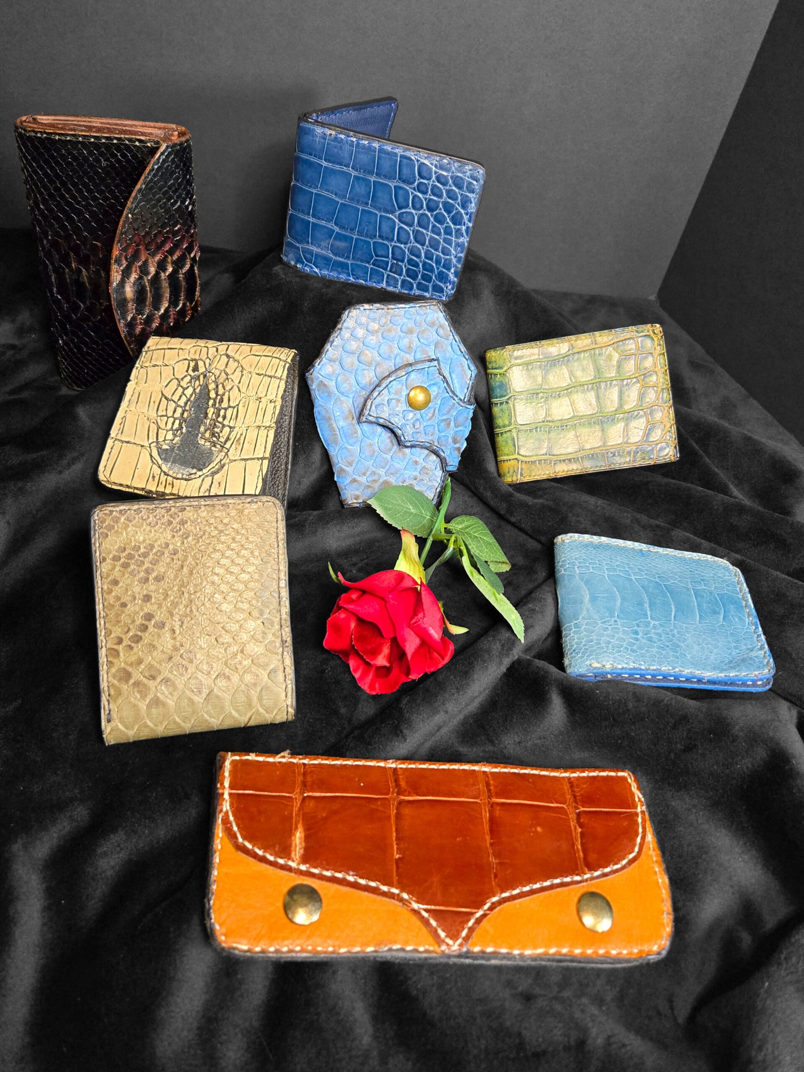 Assorted handcrafted leather wallets in various colors and textures, featuring unique designs and a rose accent, showcasing artisan craftsmanship by W.E.L.P.